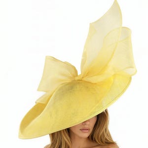 Puede incluir: Un sombrero amarillo brillante con ala ancha y un gran lazo. El sombrero tiene un dise&ntilde;o en capas con detalles de tela transparente y fluida. Un accesorio llamativo para ocasiones especiales.