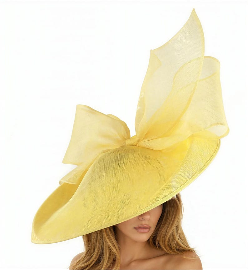 Puede incluir: Un sombrero amarillo brillante con ala ancha y un gran lazo. El sombrero tiene un dise&ntilde;o en capas con detalles de tela transparente y fluida. Un accesorio llamativo para ocasiones especiales.