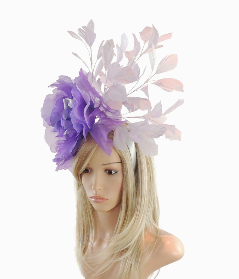 Puede incluir: Una diadema de flores de color morado y blanco con plumas. La diadema est&aacute; hecha de sat&eacute;n y tiene un dise&ntilde;o delicado y femenino.