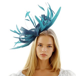 Könnte beinhalten: Ein teal-farbener Fascinator mit Federn und einer dekorativen Schleife. Der Kopfschmuck wird auf dem Kopf getragen und ist vor einem weißen Hintergrund platziert. Das Accessoire eignet sich für besondere Anlässe.