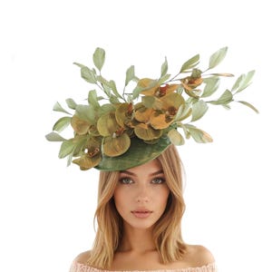 May include: A green and gold floral hat with a wide brim. The hat is adorned with large, detailed orchid-like flowers and leaves in shades of green and gold. The hat is designed for special occasions.