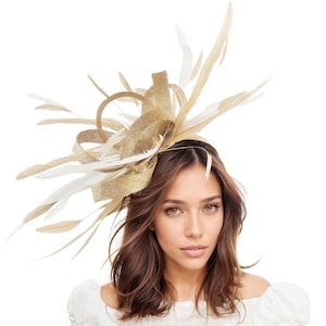 May include: A gold and cream-colored headpiece with feathers and a bow. The headpiece is worn on the head and is made of a woven material. The feathers are white and tan. The headpiece is a formal accessory.