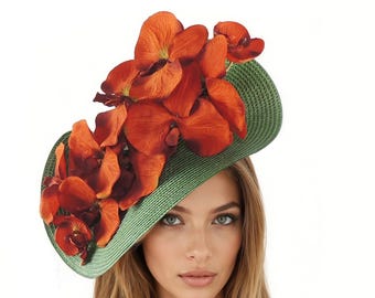 May include: A green, wide-brimmed hat decorated with large, bright orange flowers. The hat has a woven texture and a curved shape, with the flowers clustered on one side. A fashionable headpiece.