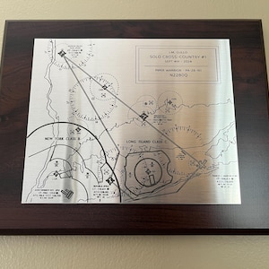 May include: A framed metal plaque with a map and text. The plaque is set in a dark brown wooden frame. The text reads "I.M. Gullo Solo Cross-Country #1 Sept 4th 2024". The map shows routes and circles.