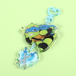 May include: A blue and green cartoon Teenage Mutant Ninja Turtle character keychain with a blue and white sword charm. The keychain has a blue metal clasp.