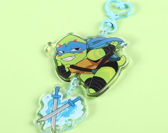 May include: A blue and green cartoon Teenage Mutant Ninja Turtle character keychain with a blue and white sword charm. The keychain has a blue metal clasp.