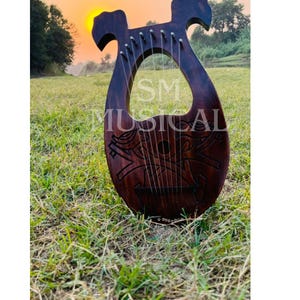 Könnte beinhalten: Eine hölzerne Leier mit dunkelbrauner Oberfläche und aufwendigen Schnitzereien. Die Leier hat 10 Saiten und liegt auf einem Bett aus grünem Gras.