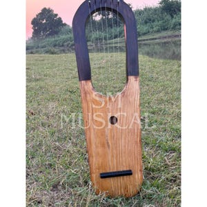 May include: A wooden lyre with a black and brown finish. The lyre has a rounded top and a flat bottom. It has multiple strings and a small sound hole.