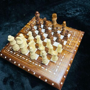 Könnte beinhalten: Ein Schachspiel aus Holz mit einem Klappbrett. Das Brett ist mit weißem Knochen eingelegt und hat eine braune Oberfläche. Die Schachfiguren sind aus Holz und im klassischen Stil gehalten.