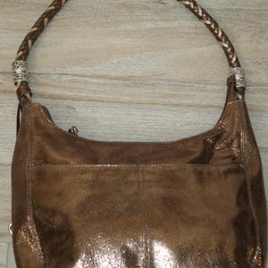 Puede incluir: Un bolso de mano de cuero de color bronce met&aacute;lico con una correa trenzada y detalles plateados.