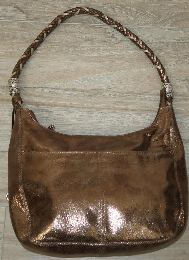 Puede incluir: Un bolso de mano de cuero de color bronce met&aacute;lico con una correa trenzada y detalles plateados.