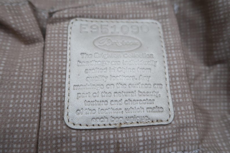 Puede incluir: Una etiqueta de cuero blanco con el texto "E951090" y "The Dilighuais Collection handbags are individually crafted in China from quality leathers. Any markings on the surface are part of the natural beauty, texture and character of the leather, which makes each bag unique."