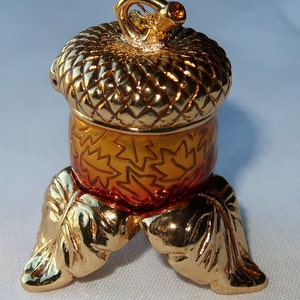 May include: A gold acorn trinket box with a detailed design of leaves. The box is on a stand with three leaf-shaped legs.