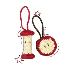 May include: Two handmade crochet apple ornaments. One is a red and cream-coloured apple core with a red loop. The other is a red and cream-coloured apple slice with a brown loop. Both have black seed details.