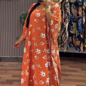 May include: A long orange maxi dress with a white floral print. The dress has a V-neckline and 3/4 sleeves. The dress has a side slit and is made of a lightweight fabric.