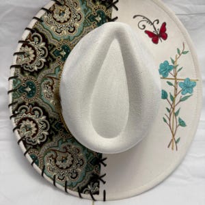 Custom hand burned ivory wide brim hat, green/brown/gold fabric with black leather lacing and blue flowers/gold cross painted on brim.