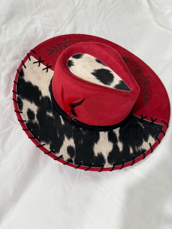 Red wide brim hat, black/white cowhide fabric, flowers burned on brim, black band, red/black feathers, black leather lacing.