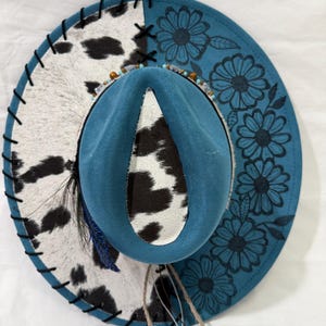 Custom hand burned ocean blue wide brim hat, black and white cowhide fabric with black leather lacing and flowers burned on brim.