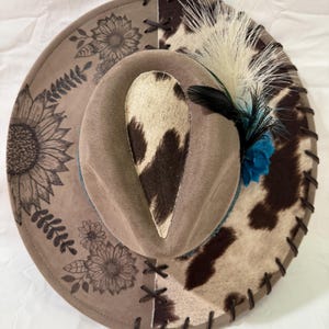 Custom hand burned mocha wide brim hat, brown/white cowhide fabric with brown leather lacing and sunflowers burned on brim, blue hat band.