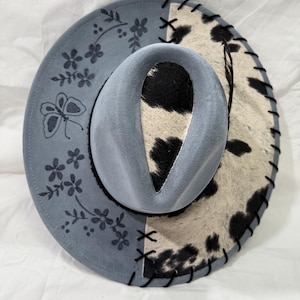 Custom hand burned denim blue wide brim hat, black/white cowhide fabric with black leather lacing and flowers/butterfly burned on brim.