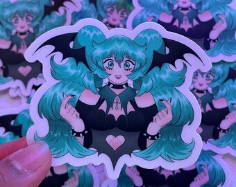 May include: A sticker featuring a cartoon character with green hair, bat wings, and a black and white outfit. The character is wearing a heart-shaped necklace and has a heart-shaped design on their chest. The sticker is on a white background.