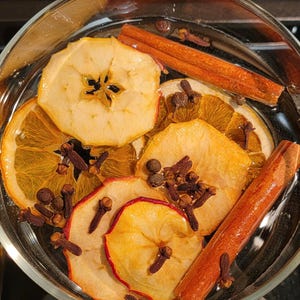 May include: A glass bowl filled with water and various ingredients for a potpourri, including dried apple slices, orange slices, cinnamon sticks, and cloves.