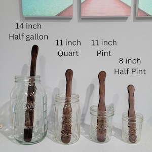 Peut inclure: Quatre bocaux en verre avec des cuillères en bois à l'intérieur. Les bocaux sont étiquetés avec leur taille : 14 pouces Demi-gallon, 11 pouces Quart, 11 pouces Pinte, et 8 pouces Demi-pinte.