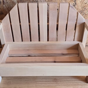 Może przedstawiać: Mała, nieoszlifowana drewniana sofa z oparciem z listew i prostokątnym siedziskiem. Sofa wykonana jest z jasnego drewna i ma prosty design.