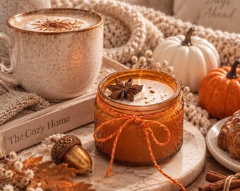 May include: A scented candle in an amber glass jar with a textured surface, tied with an orange and yellow twine bow. The candle features a white wax surface topped with a single star anise and a lit wick, resting on a round marble tray.