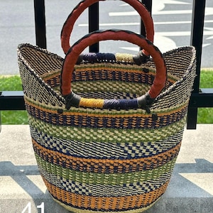 May include: A woven basket featuring horizontal stripes in shades of orange, green, blue, and natural tan. The basket has two rounded handles wrapped in a reddish-brown material with black accents. The number 41 is printed in white in the bottom corner.
