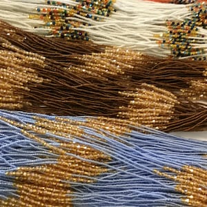 May include: Three strands of multi-strand beaded necklaces featuring thin threads in white, brown, and light blue. Each strand is accented with small, reflective, faceted beads arranged in repeating geometric patterns along the length of the cords.