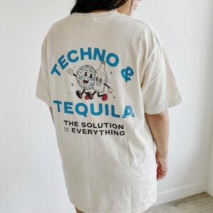 Puede incluir: Camiseta color crema con las palabras "TECHNO & TEQUILA" en azul, junto con un dibujo animado de una bola de discoteca y una botella de tequila. El texto "THE SOLUTION TO EVERYTHING" est&aacute; impreso debajo en negro.