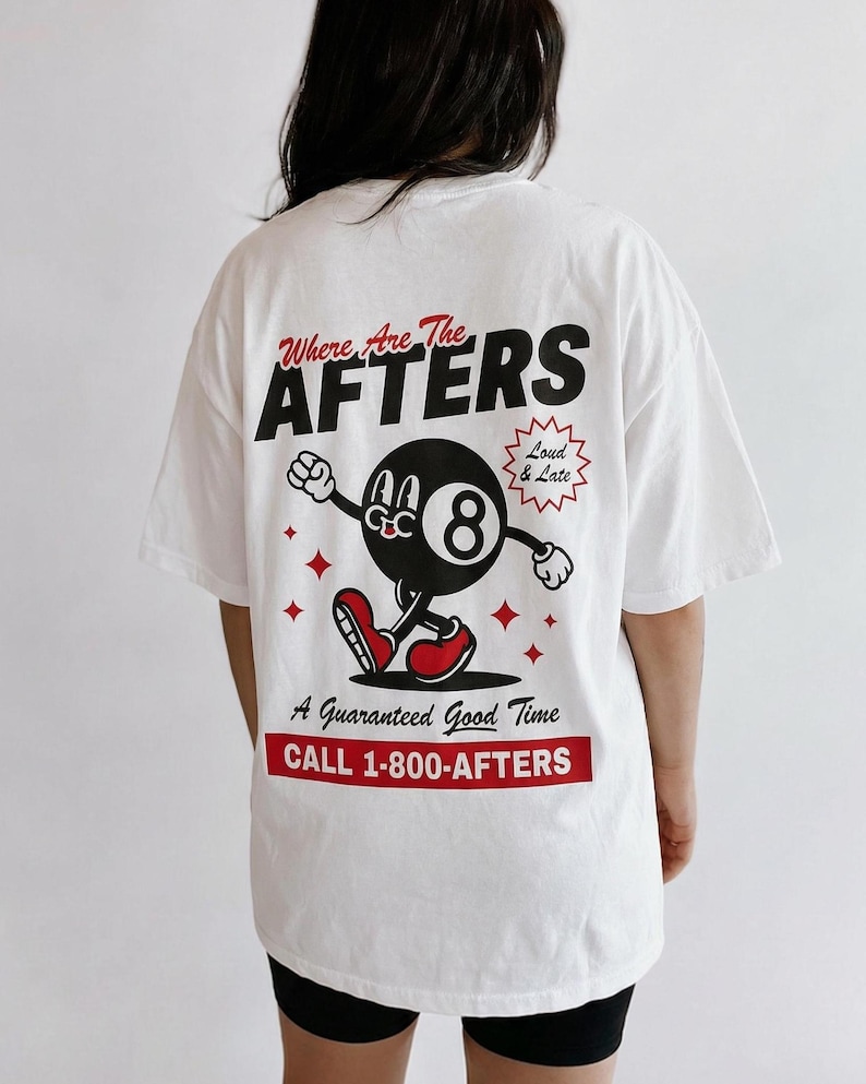 A girl with dark hair wearing a white shirt. She is facing away from the camera. On the back of the shirt is a cartoon Eight Ball and the text “where are the AFTERS” “A guaranteed good time” “CALL 1-800-AFTERS”