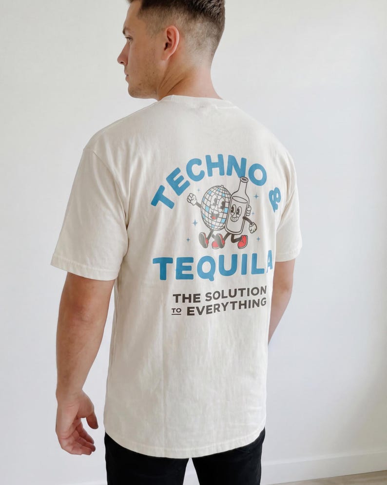 Puede incluir: Camiseta color crema con un gr&aacute;fico en la espalda que presenta una bola de discoteca y una botella de tequila de dibujos animados. El texto dice "TECHNO & TEQUILA" y "THE SOLUTION TO EVERYTHING" en azul. La camiseta tiene mangas cortas.