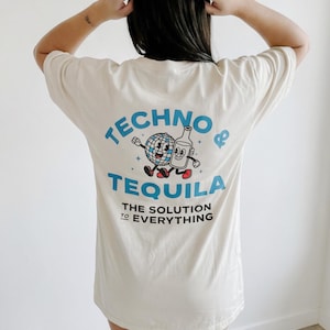 A girl with dark hair wearing a cream shirt. She is facing away from the camera. On the back of the shirt is a cartoon globe and tequila bottle walking together. the main text says “TECHNO & TEQUILA” with sub-text reading “THE SOLUTION TO EVERYTHING”