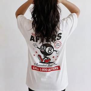May include: White t-shirt with a graphic on the back featuring a cartoon eight ball character with red shoes and arms outstretched. The text reads "Wants AFTERS" and "A Guaranteed Good Time CALL 1-800-AFTERS."