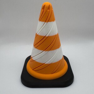 May include: A small orange and white traffic cone with a black base. The cone has a spiral pattern.