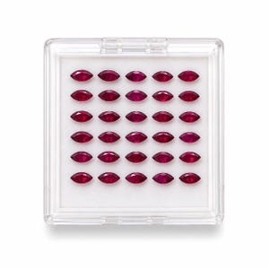 May include: A clear plastic case filled with thirty-two marquise-cut, deep red gemstones. The gems are arranged in a grid pattern on a white background. The case is rectangular with a hinged lid, and the gems are evenly spaced.