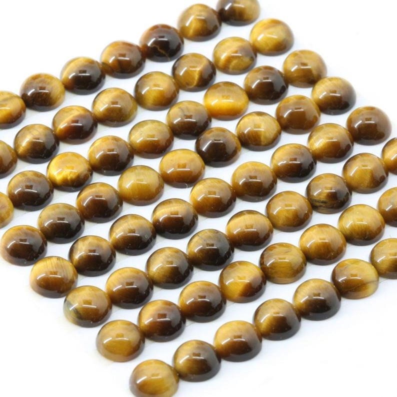 May include: A collection of polished, round tiger's eye gemstones. The stones display a mix of golden brown and dark brown hues, with a chatoyant effect. The gemstones are arranged closely together, creating a visually appealing pattern.