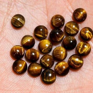 May include: A collection of polished, round tiger's eye gemstones. The stones display a mix of golden brown and dark brown colors with chatoyancy, creating a shimmering effect. The gemstones are smooth and spherical.