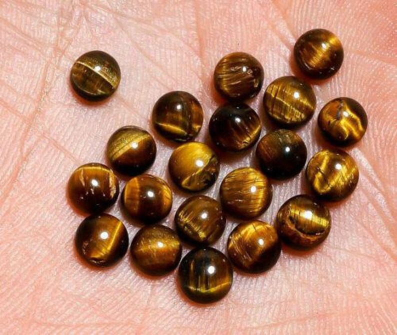 May include: A collection of polished, round tiger's eye gemstones. The stones display a mix of golden brown and dark brown colors with chatoyancy, creating a shimmering effect. The gemstones are smooth and spherical.