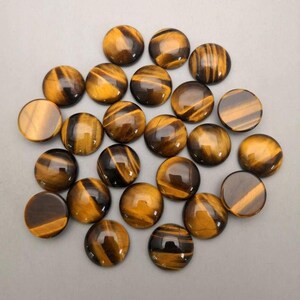 May include: A collection of twenty-one round tiger's eye gemstones. The stones are polished, displaying a mix of golden brown and dark brown bands. The gemstones are arranged on a light gray surface.