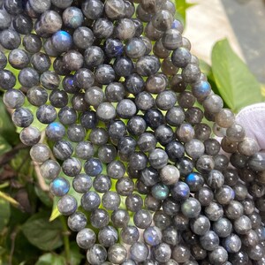 May include: A strand of round, dark gray labradorite beads with iridescent blue and green flashes. The beads are smooth and polished.