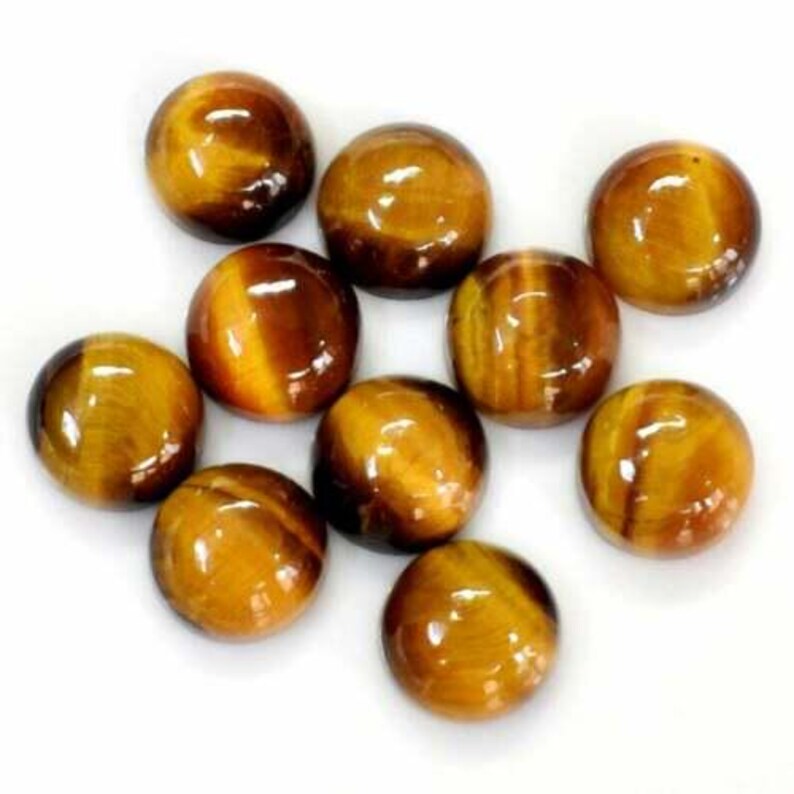 May include: A collection of ten polished tiger's eye gemstones. The stones are round, with a glossy finish and a mix of golden-brown and dark brown colors. The gemstones are arranged on a white surface.