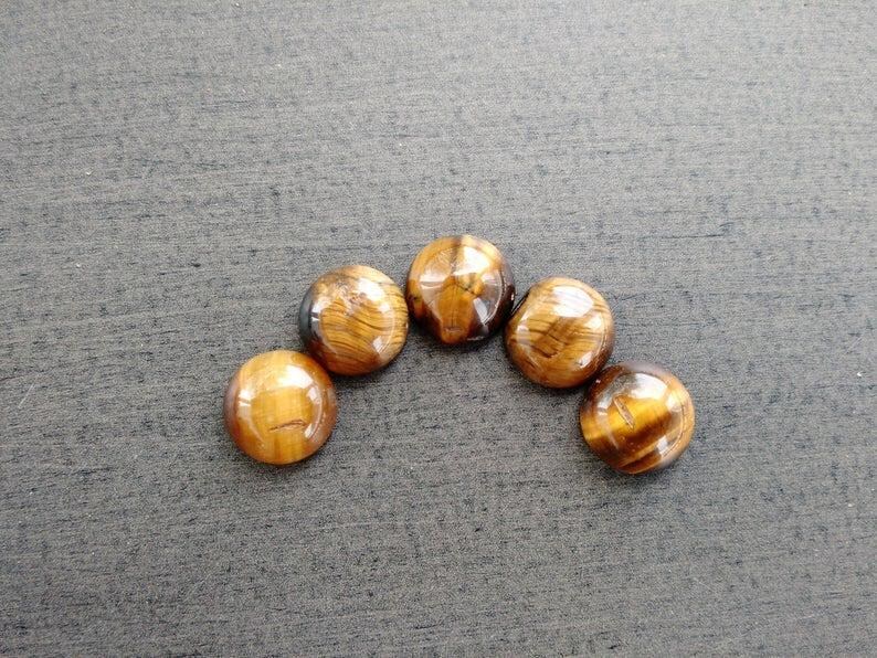 May include: Five polished tiger's eye gemstones arranged in a semi-circle. The stones display a warm, golden-brown color with distinctive bands and patterns. The gemstones are smooth and rounded, with a glossy finish.