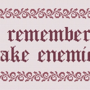 Op de afbeelding: Een beige cross-stitch sampler met een bordeauxrode rand en twee gouden leeuwen aan weerszijden. De tekst luidt "be remembered make enemies".