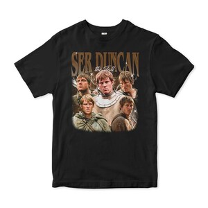 May include: Black t-shirt featuring a vintage-style graphic of a man in various poses, with the text "Ser Duncan the Tall" in gold lettering. The design includes multiple images of the same person, creating a collage effect.