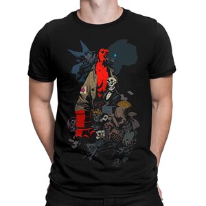 Może przedstawiać: Czarny t-shirt z grafiką w stylu komiksowym. Projekt przedstawia czerwoną postać z rogami, płaszczem i papierosem, otoczoną czaszkami i kartami do gry.