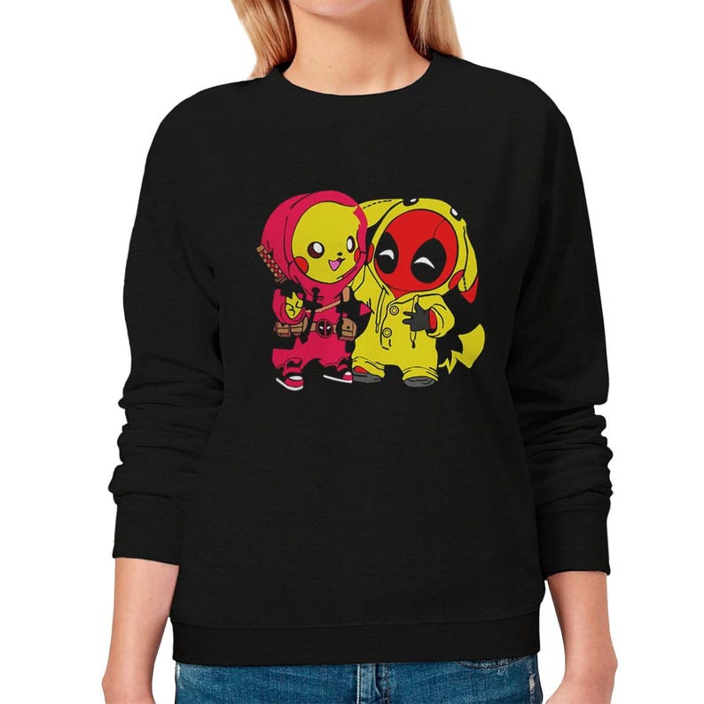 Puede incluir: Sudadera negra con una ilustraci&oacute;n de dibujos animados de dos personajes. Un personaje viste un atuendo rojo y rosa, y el otro un atuendo amarillo y rojo. Los personajes est&aacute;n uno al lado del otro.