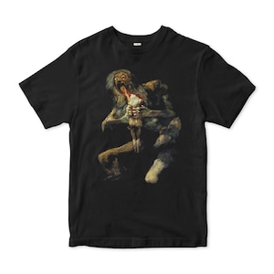 Puede incluir: Camiseta negra con una pintura de una escena perturbadora. La obra de arte muestra una figura humanoide pálida y musculosa con pelo largo y la boca abierta, devorando a otra figura. El diseño es una ilustración oscura y macabra.